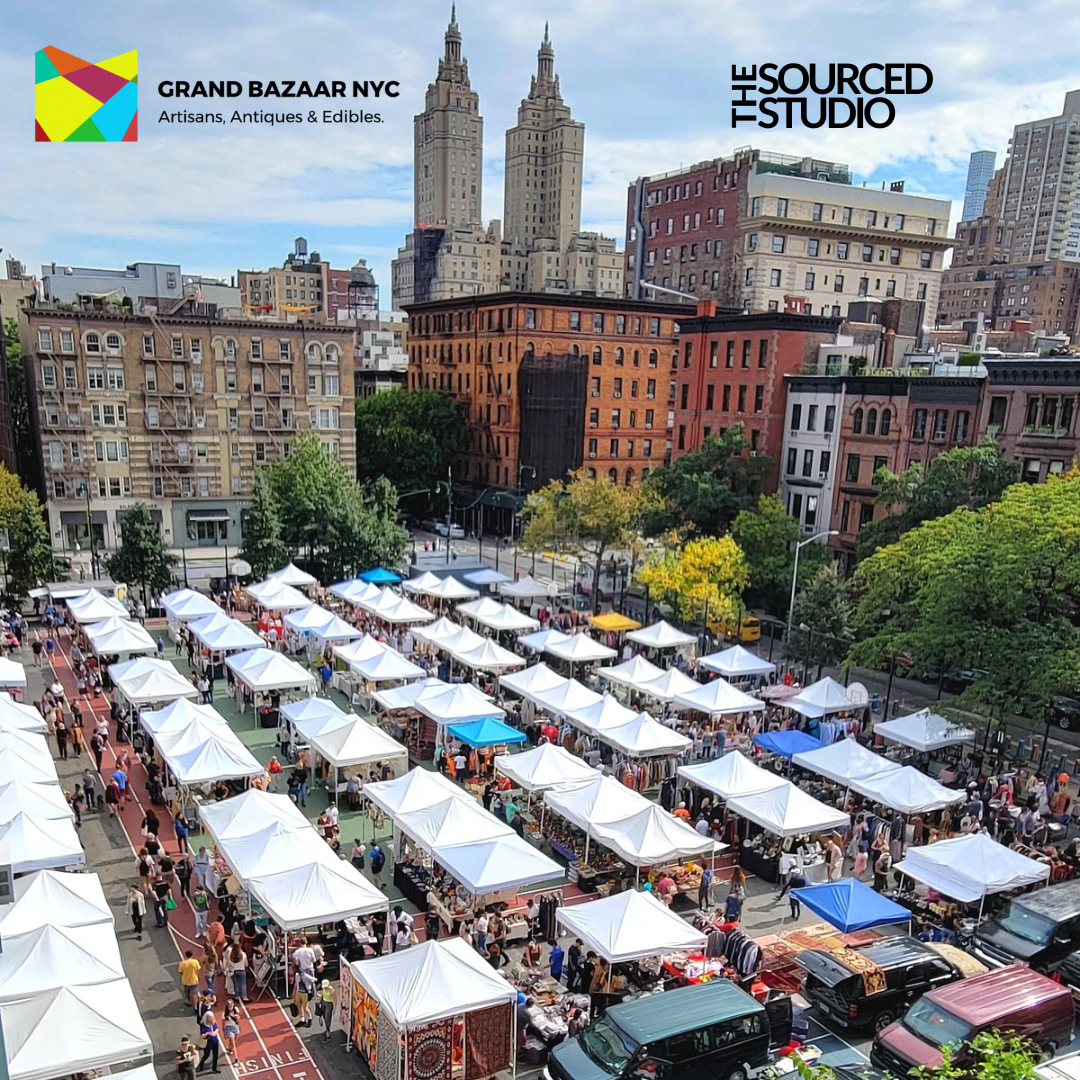 Aerial view of Grand Bazaar NYC outdoor market with rows of white vendor tents and a crowd of shoppers, set against a backdrop of Upper West Side buildings. Logos for Grand Bazaar NYC and The Sourced Studio appear in the corners.