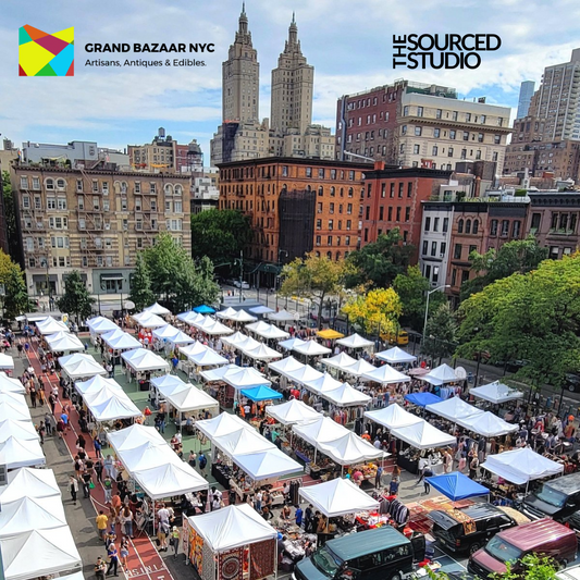 Aerial view of Grand Bazaar NYC outdoor market with rows of white vendor tents and a crowd of shoppers, set against a backdrop of Upper West Side buildings. Logos for Grand Bazaar NYC and The Sourced Studio appear in the corners.