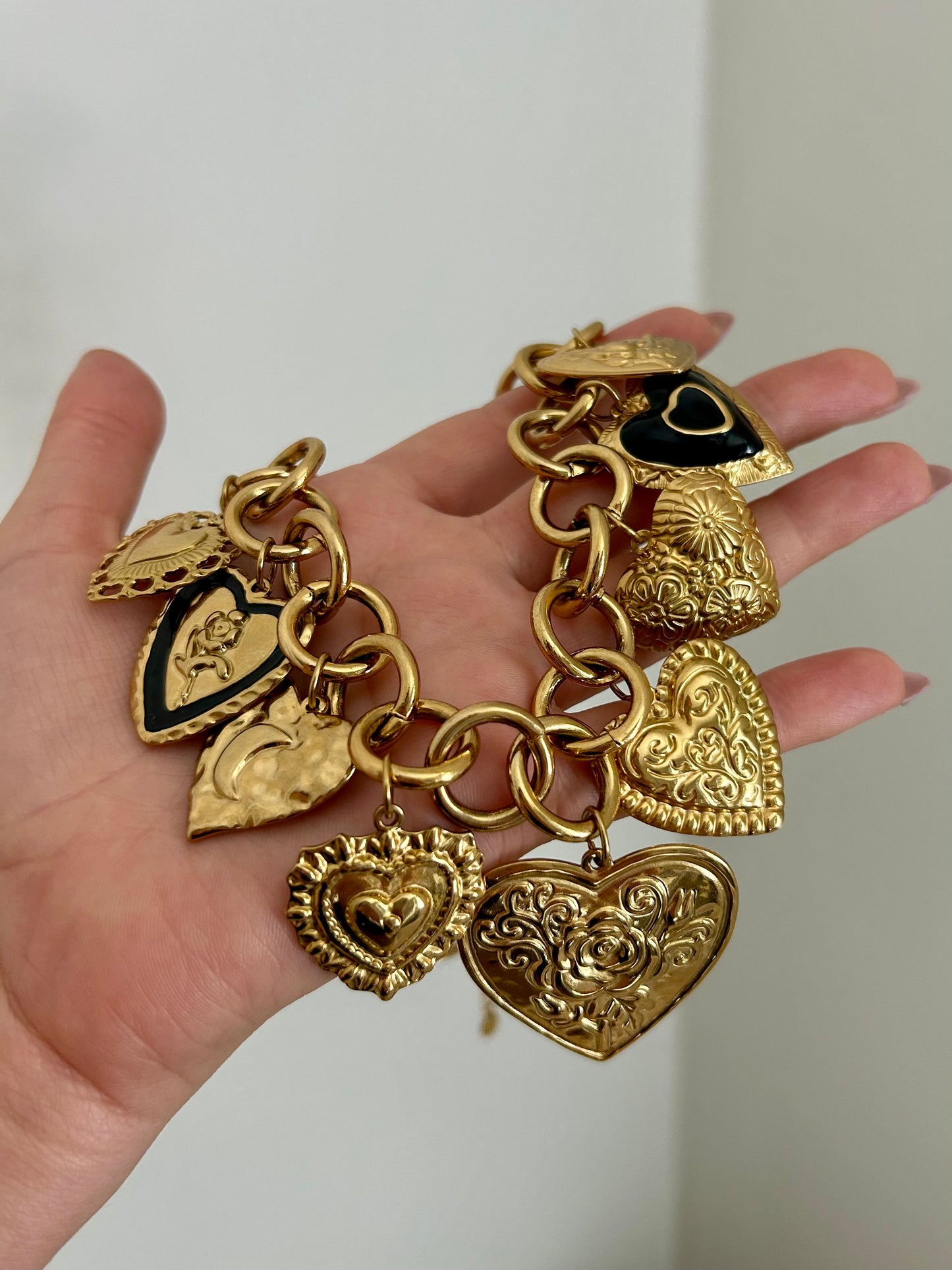 Gold charm bracelet with heart-shaped pendants held in a hand against a neutral background