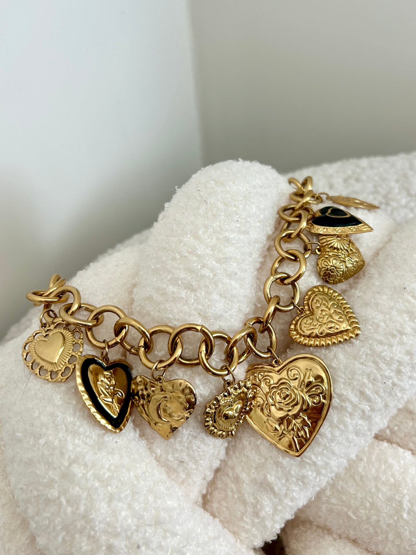 Gold charm bracelet with heart-shaped charms on a white fabric background