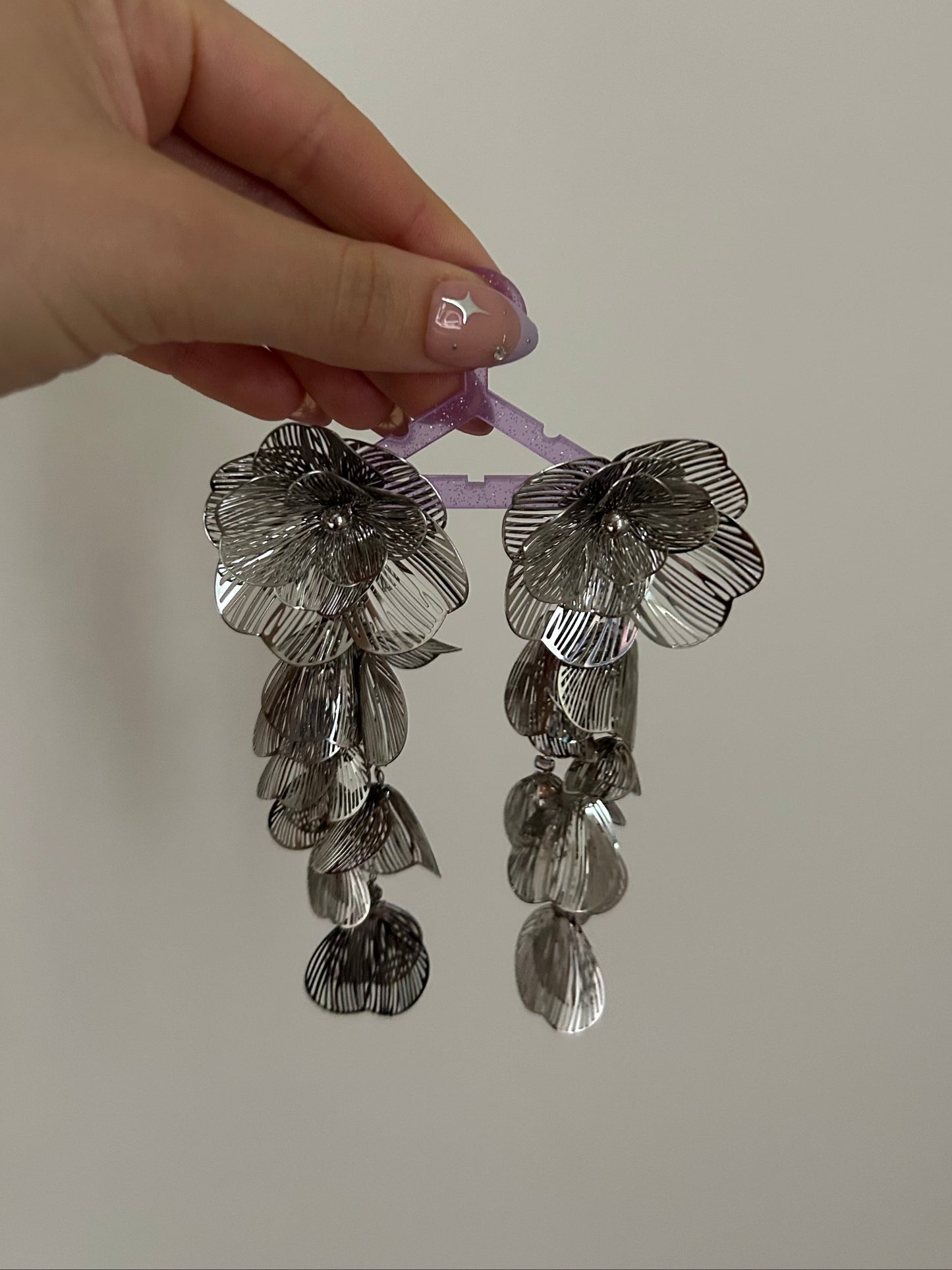 Hand holding a pair of floral earrings against a plain background
