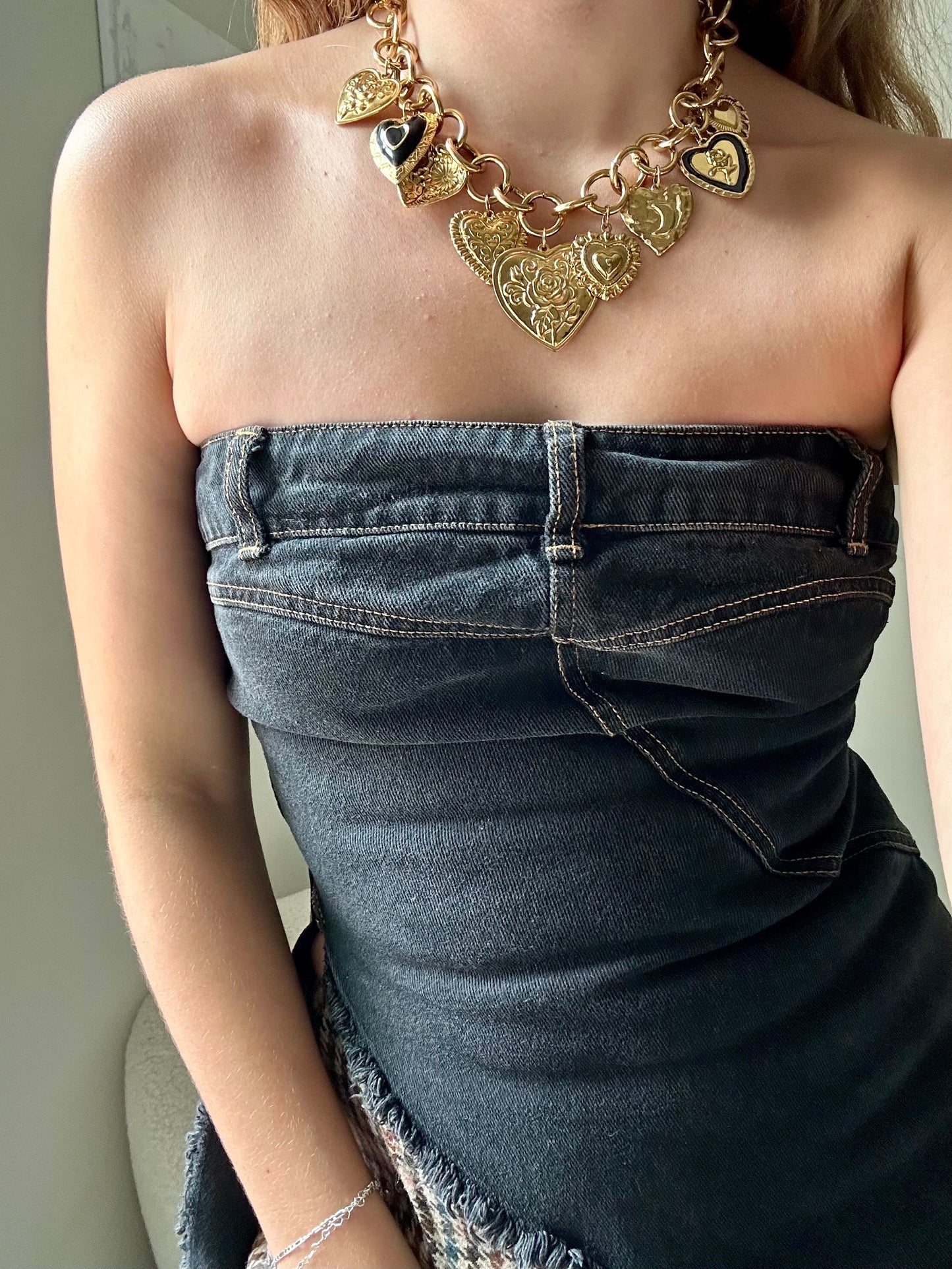 Person wearing a gold necklace and denim strapless top against a neutral background