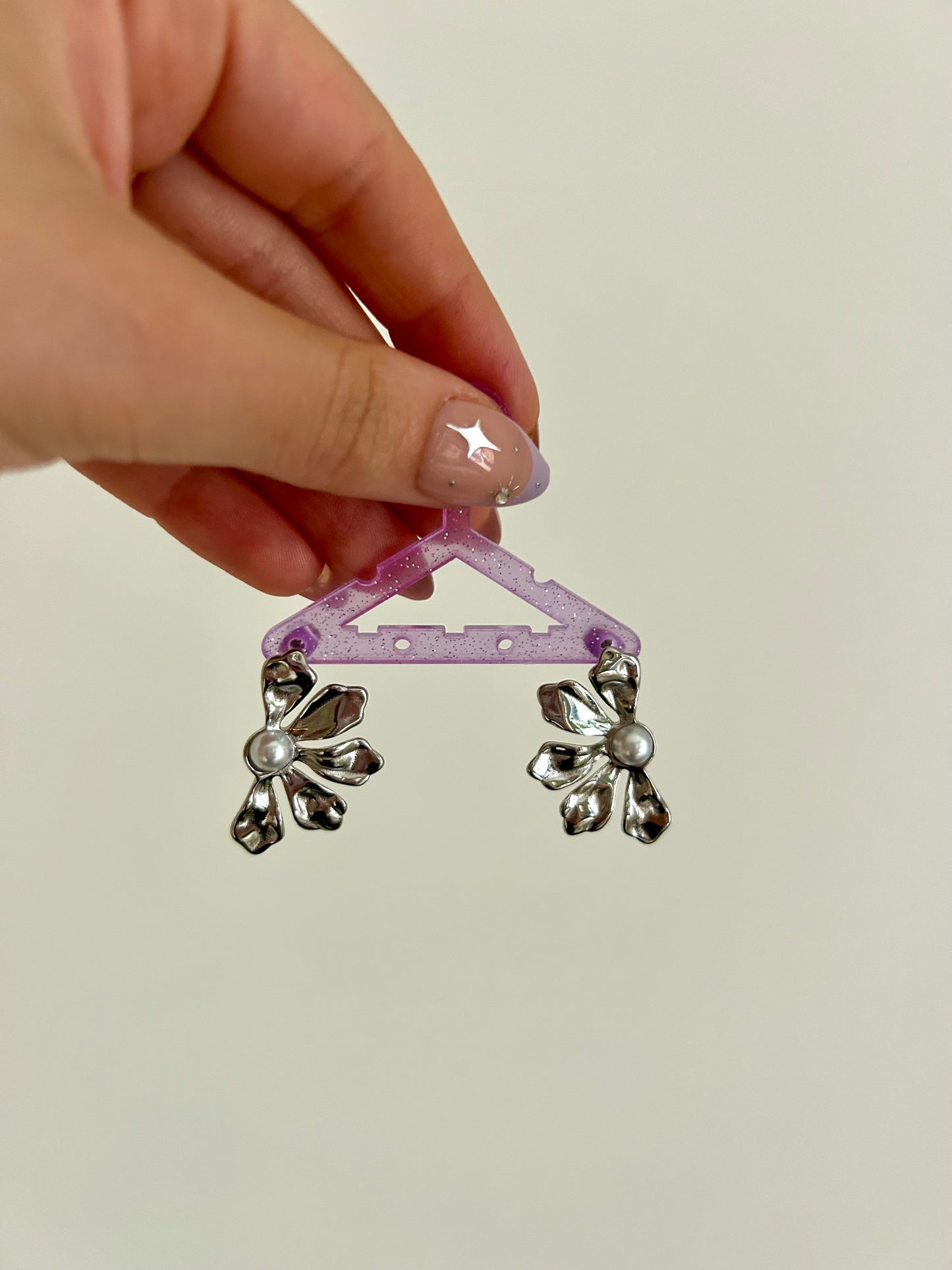 Hand holding a small pink plastic hanger with silver floral attachments against a plain background
