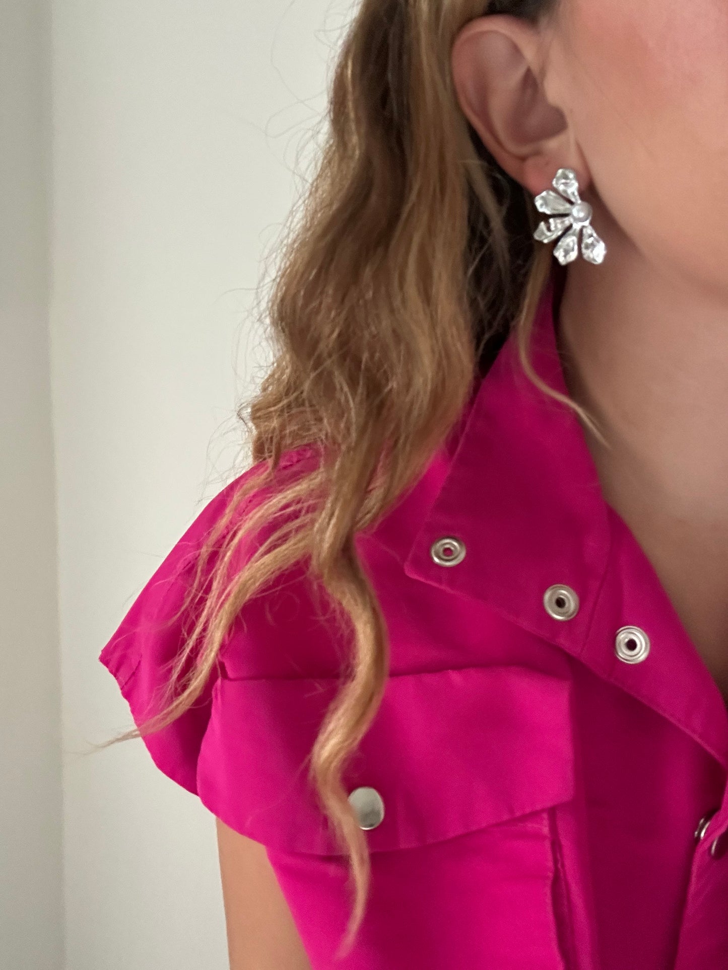 Close-up of a person wearing a pink jacket with silver buttons and a silver earring.