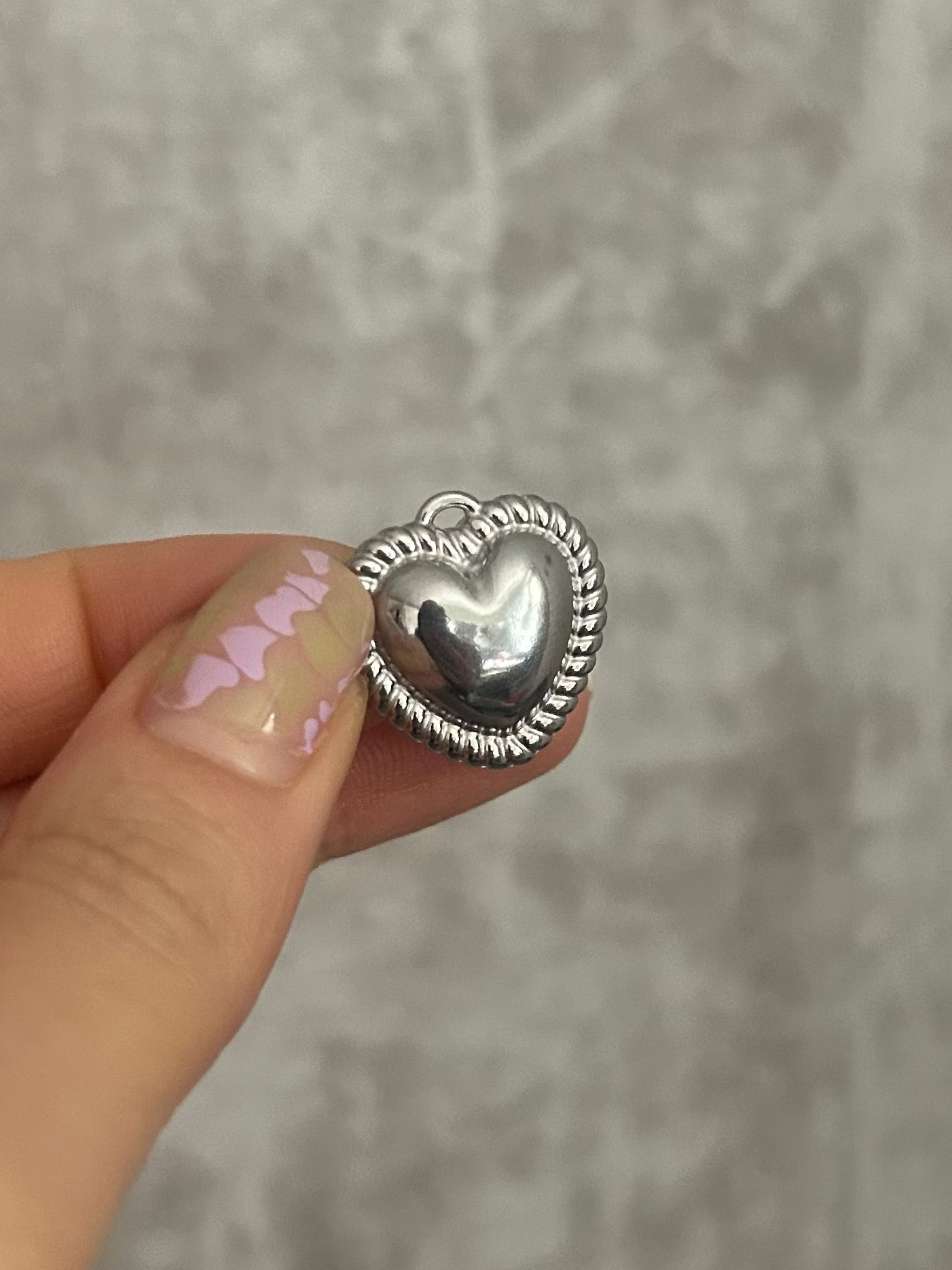 Silver heart-shaped object held by a hand against a gray background