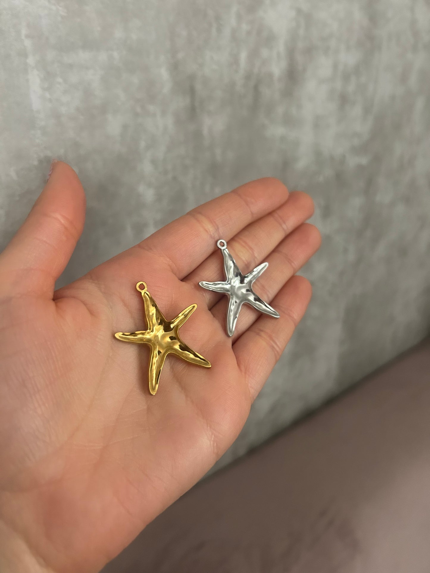 Gold and silver star-shaped pendants held in a hand against a neutral background