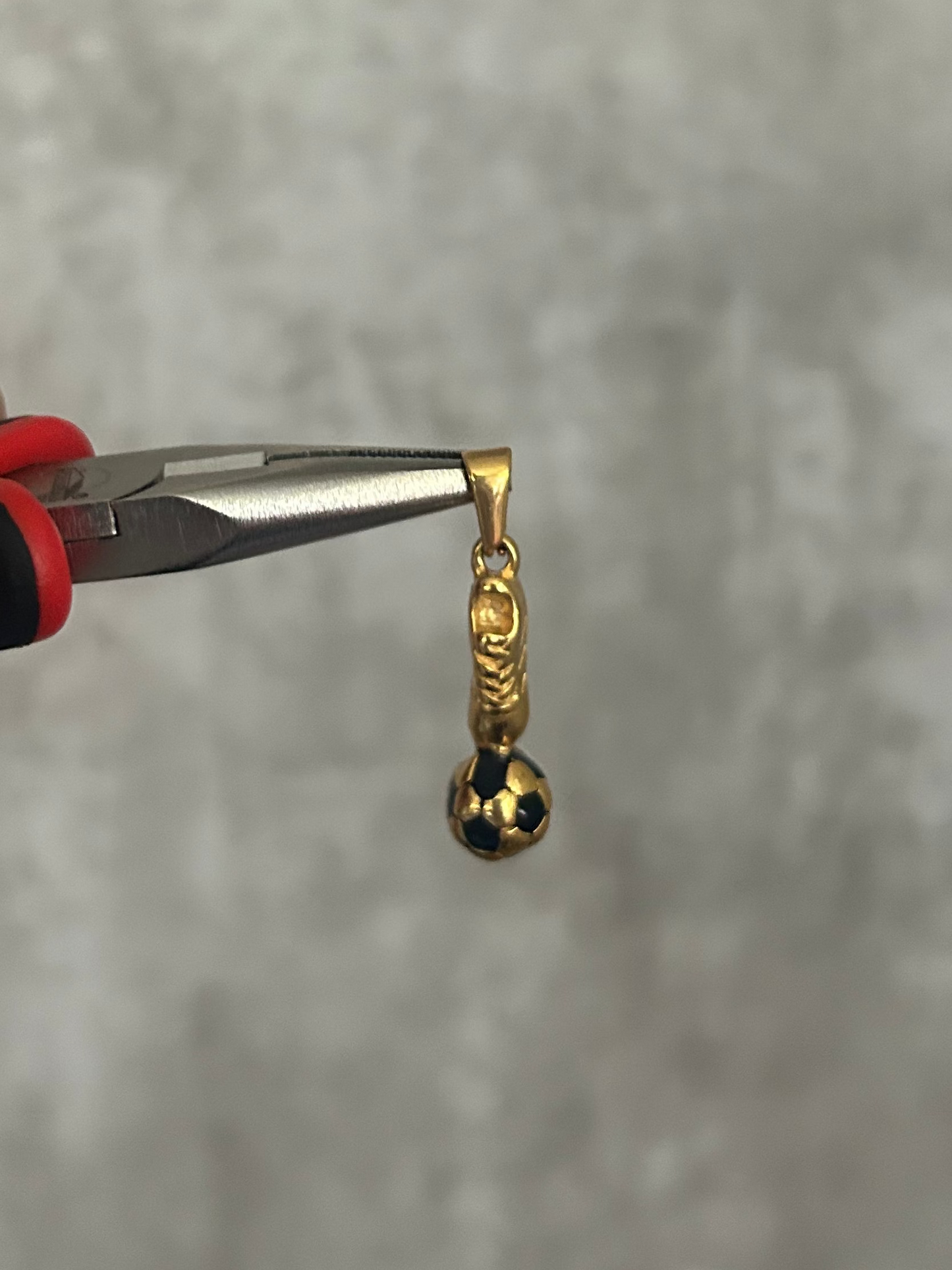 Gold earring being held by a pair of pliers against a gray background