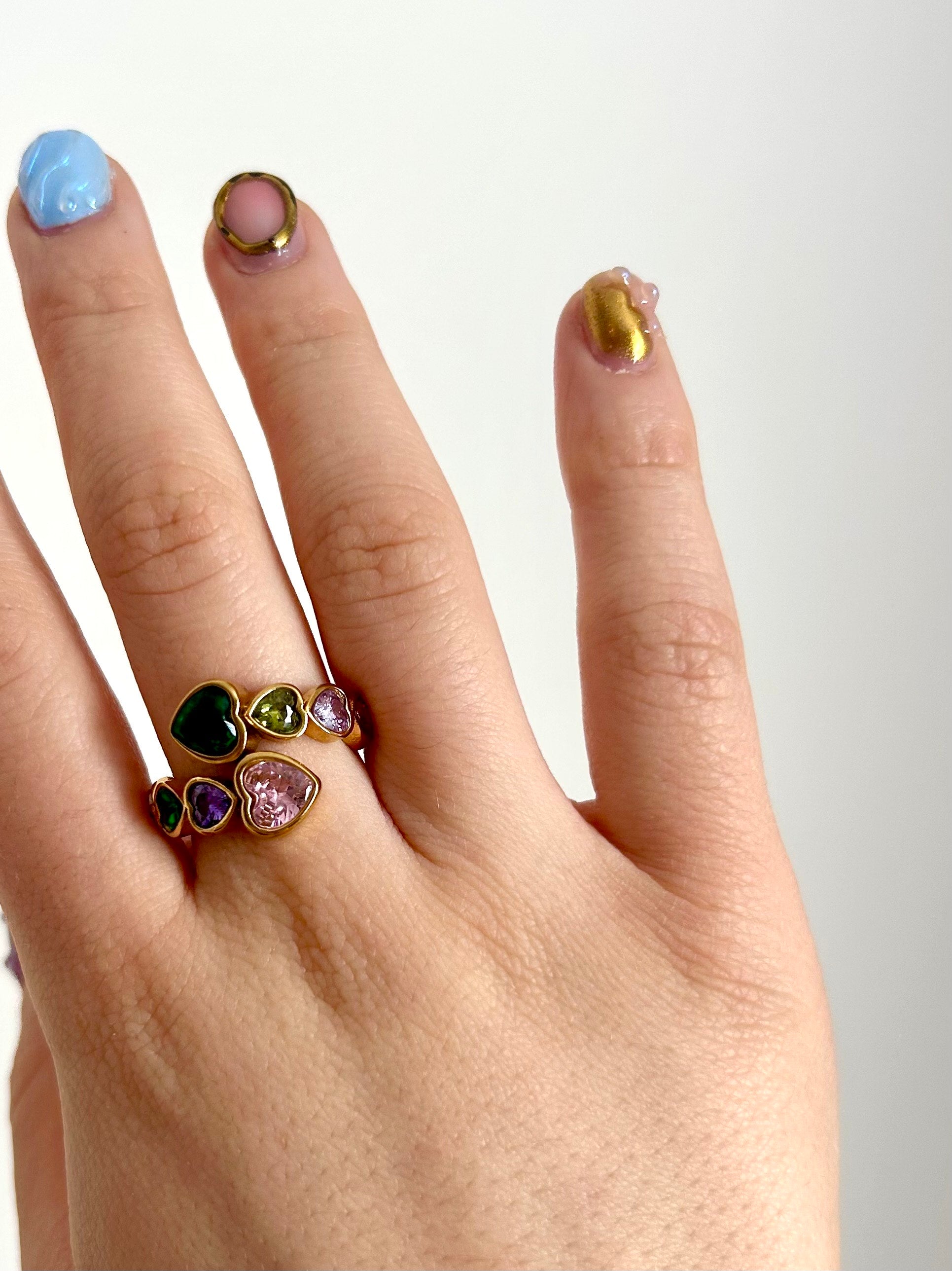 Hand modeling rainbow heart ring in sunlight – colorful reflective stones