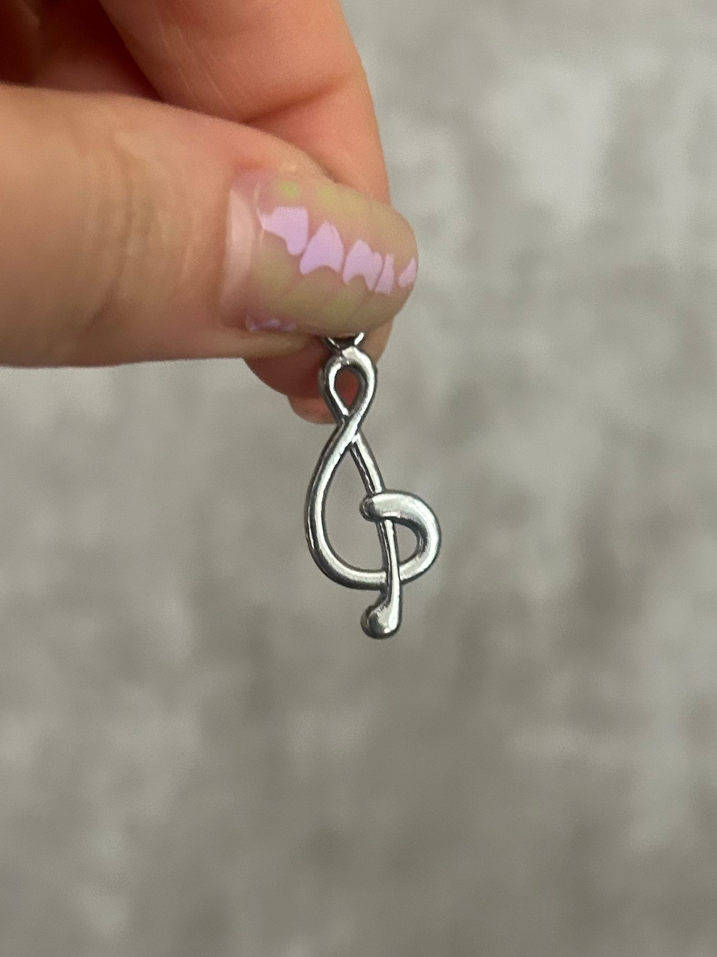 Silver music note charm held by a hand against a gray background