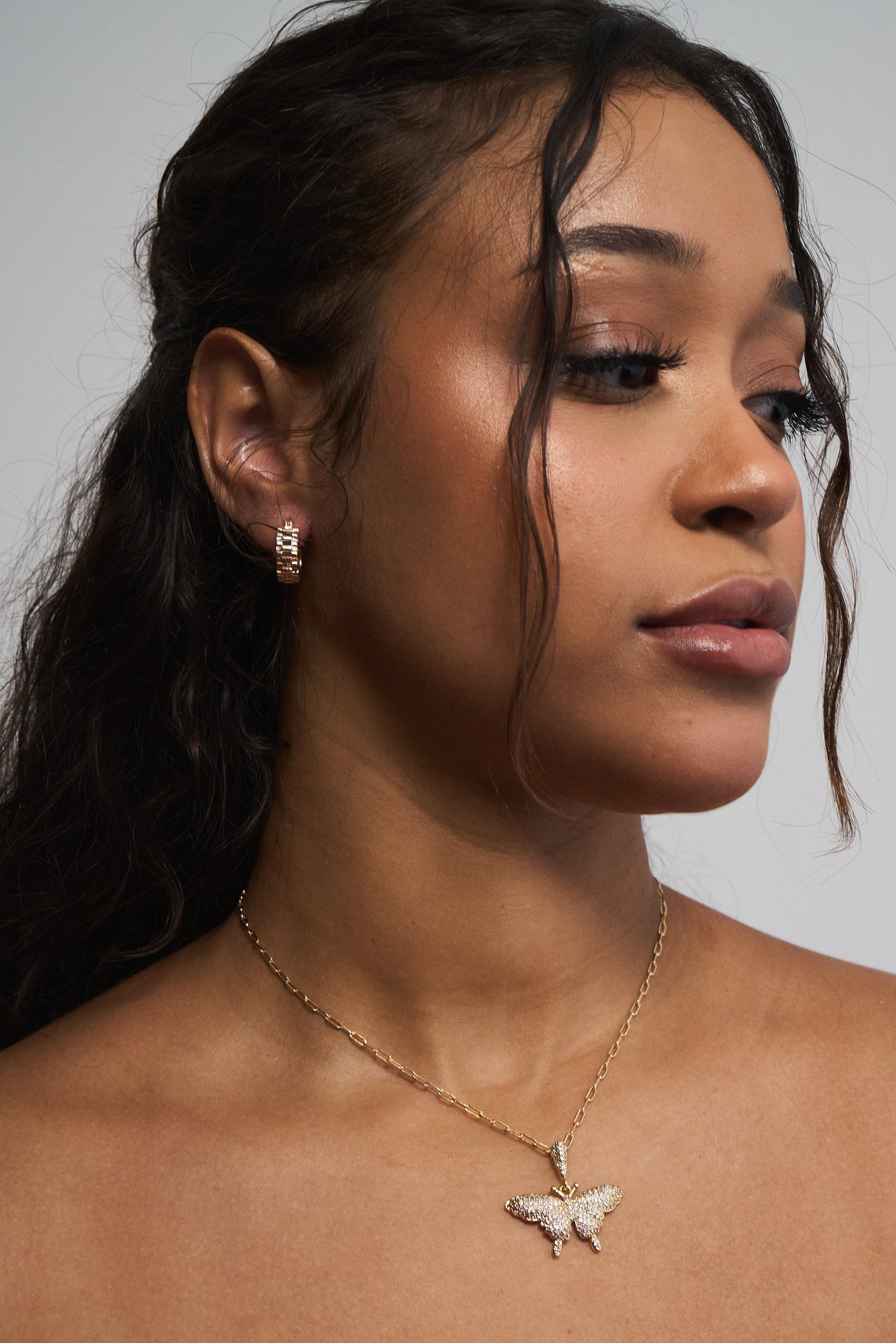 Close-up of gold watch band hoop earrings on neutral background