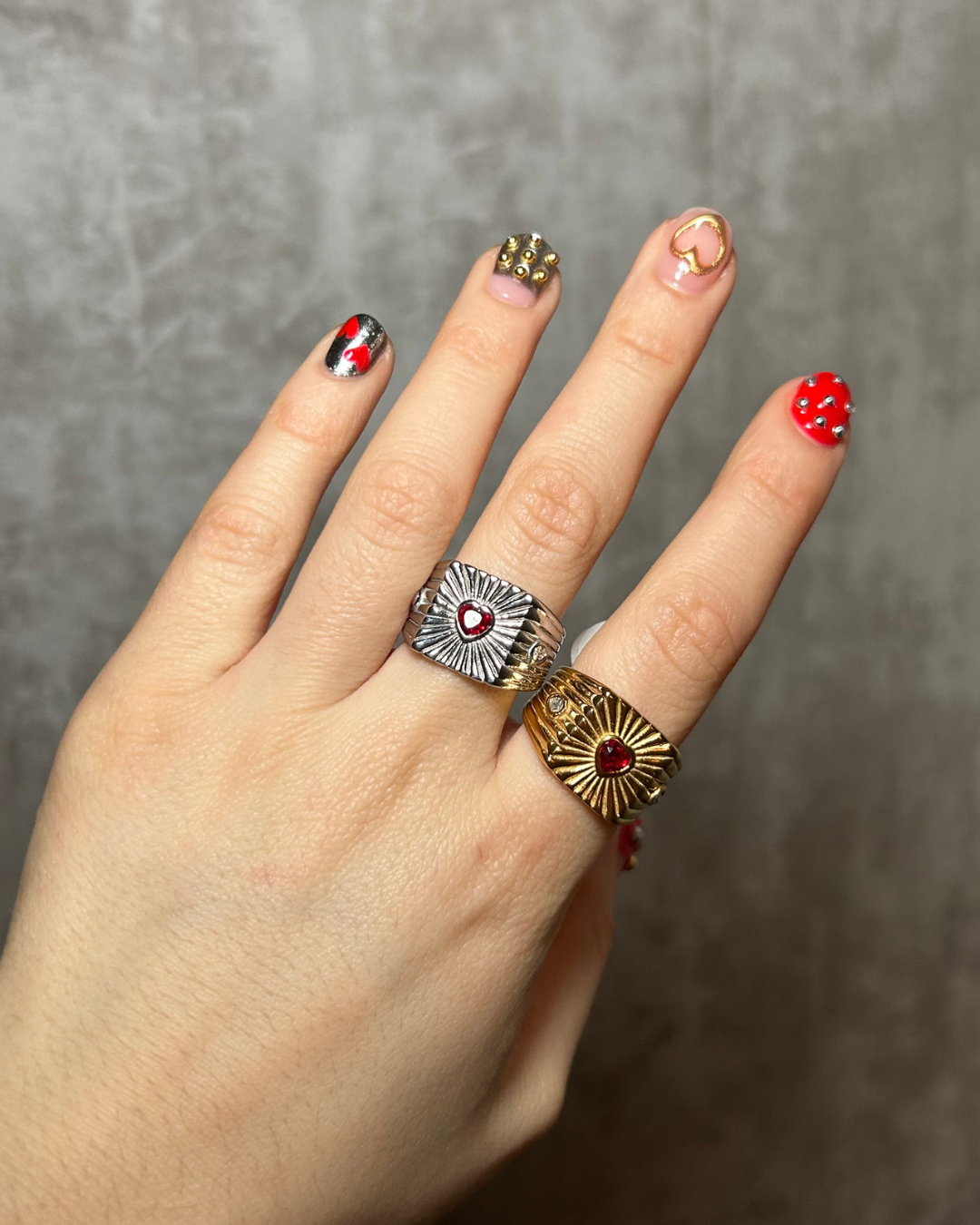 Hand wearing two rings with red gemstones against a neutral background