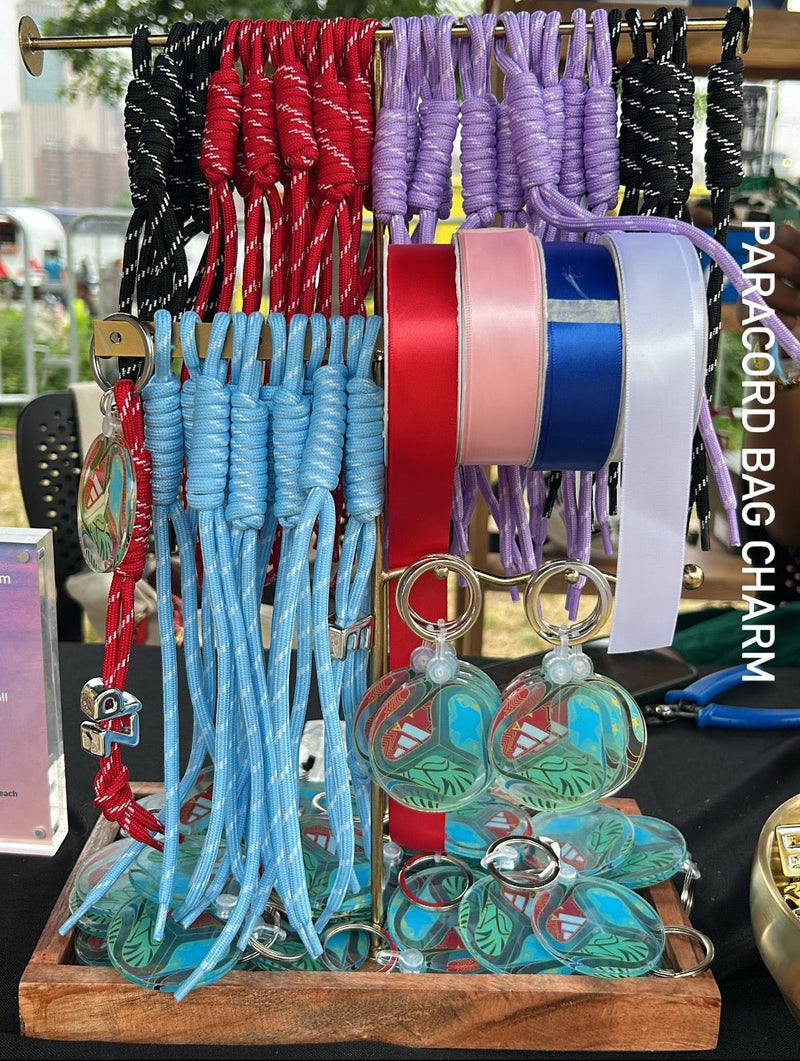 Colorful paracord bags and keychains on a wooden stand with an Adidas sign in the background.