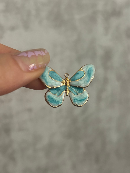 Blue butterfly-shaped earring held between fingers against a gray background