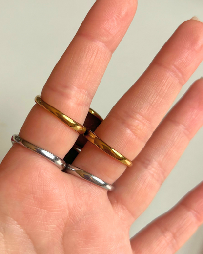 Gold and silver rings on a person's finger against a plain background