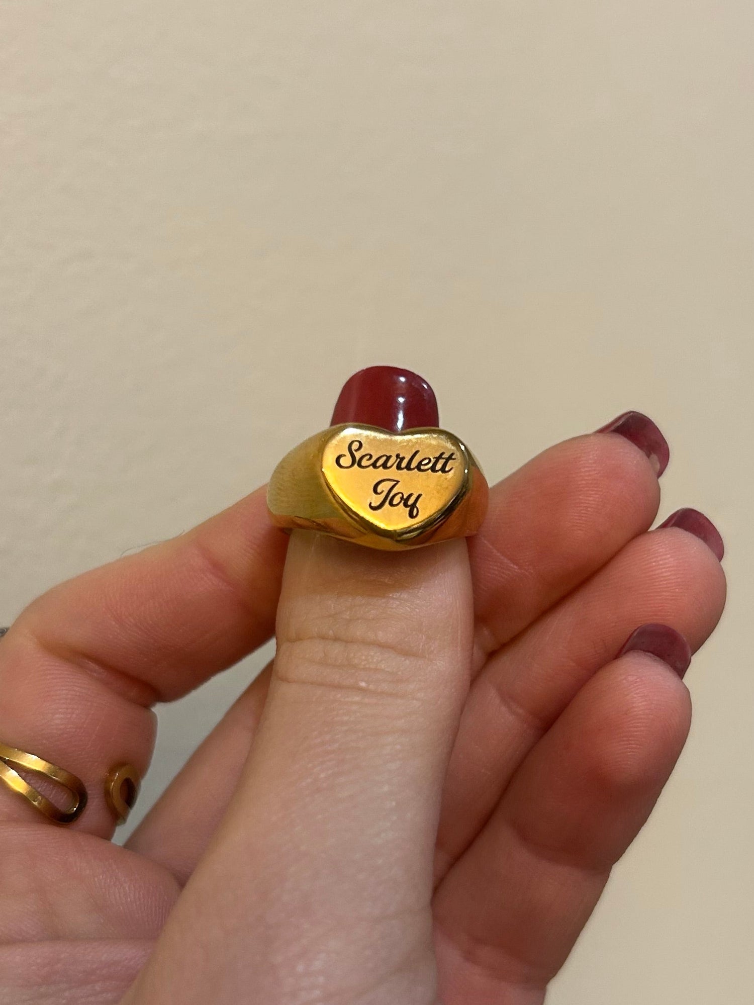 Hand wearing a gold ring with custom engraving on a neutral background