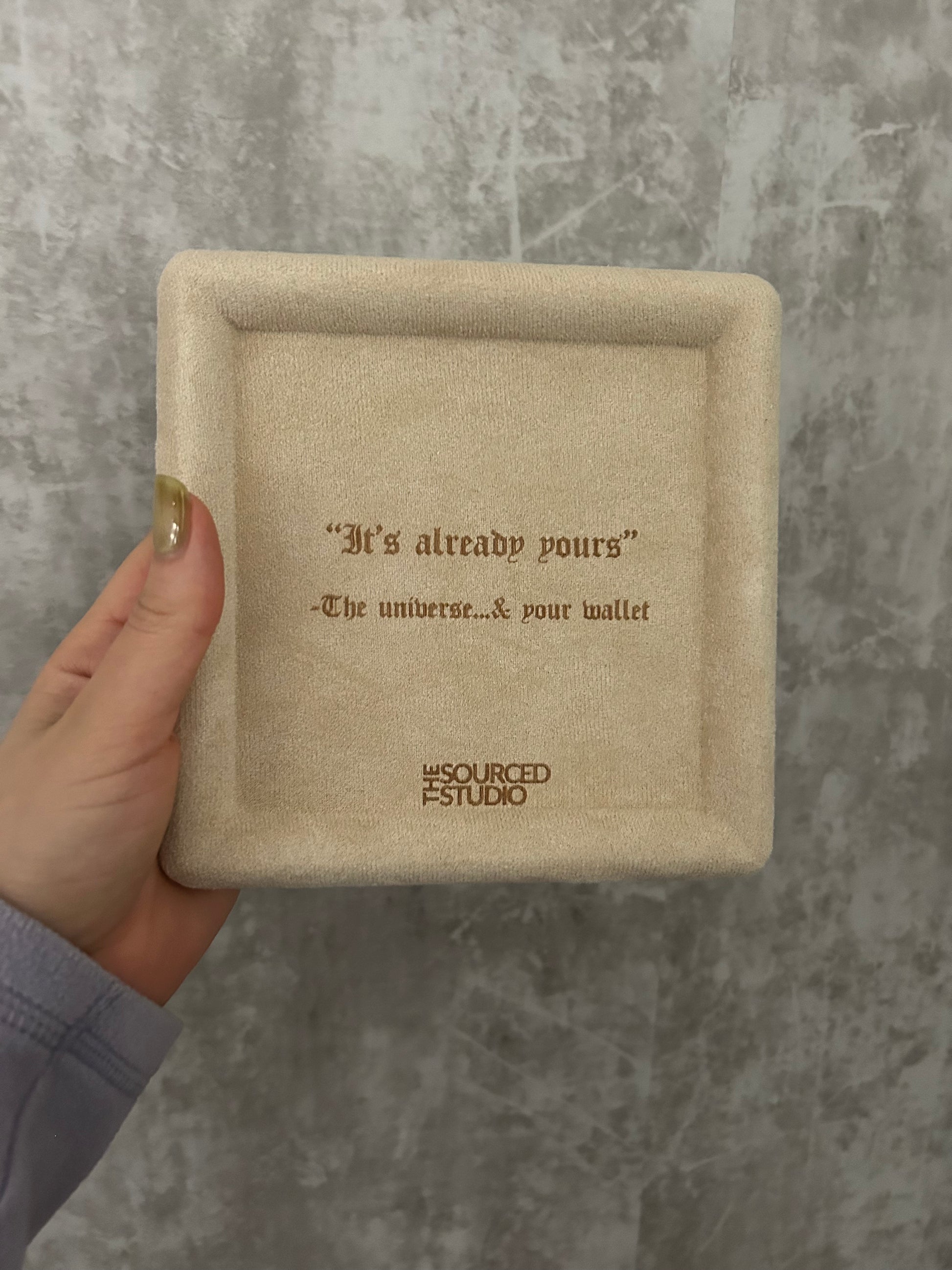 Beige jewelry box with text held by a hand on a gray surface