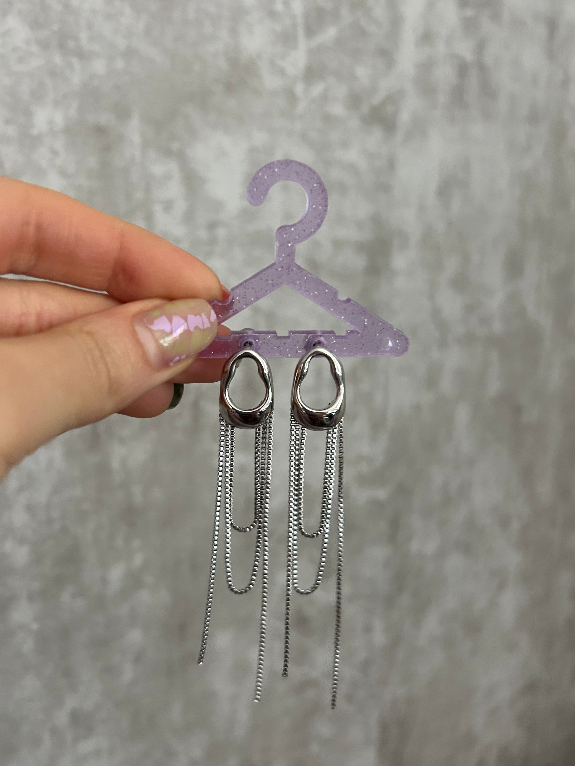 Silver chain earrings on a small purple hanger against a gray background