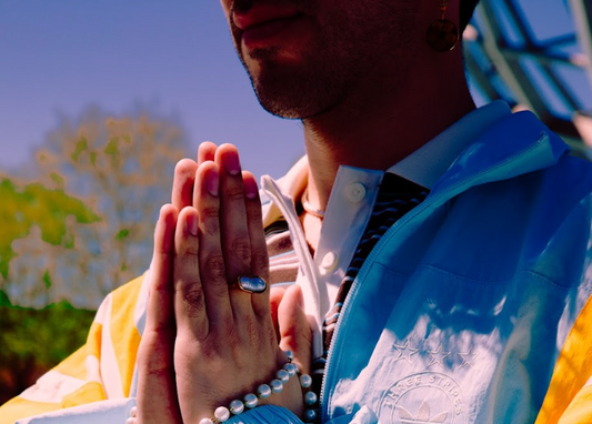 Person wearing a blue jacket with a logo, sitting outdoors with trees in the background
