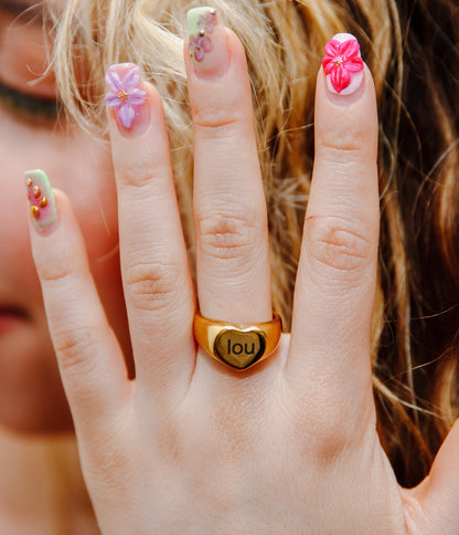 Close-up of engraved name ring on woman’s hand with pink nails