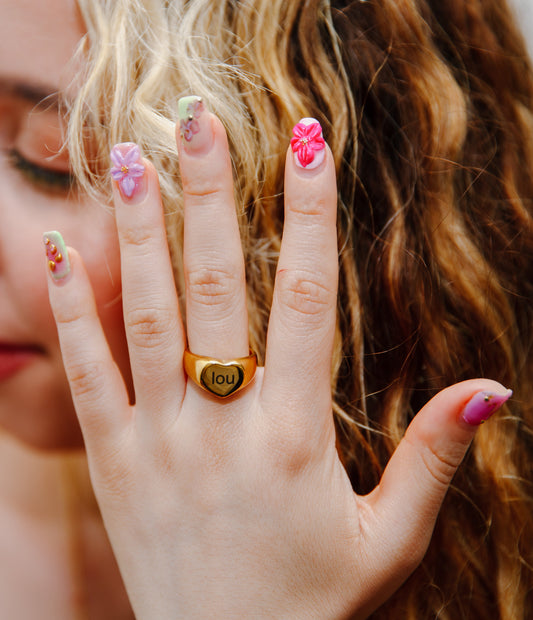 Close-up of engraved name ring on woman’s hand with pink nails