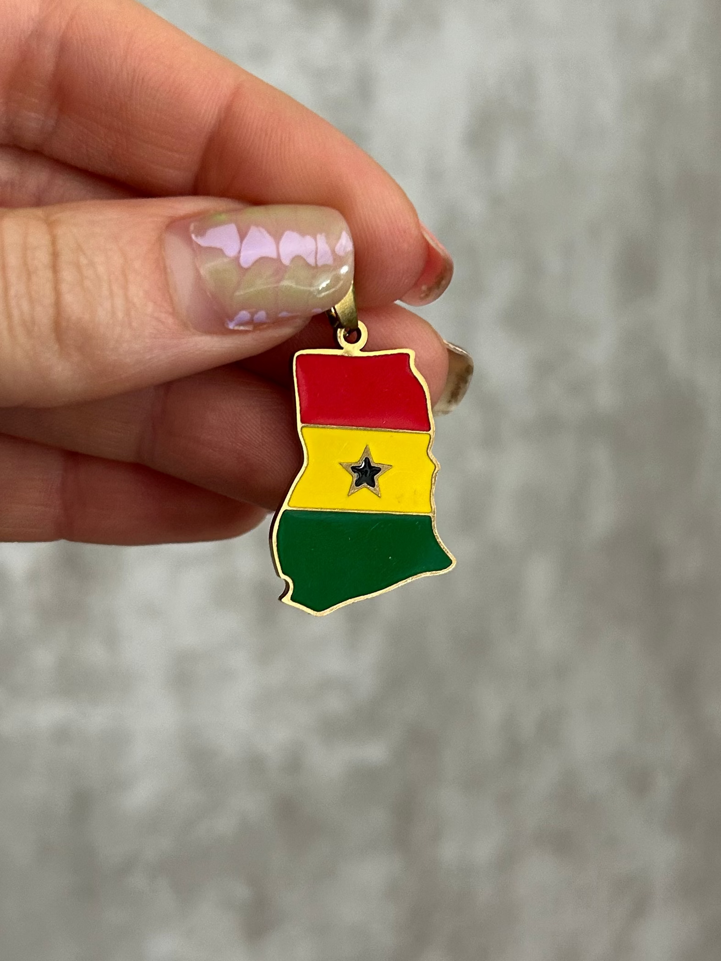 Hand holding a small pendant with a colorful design against a neutral background