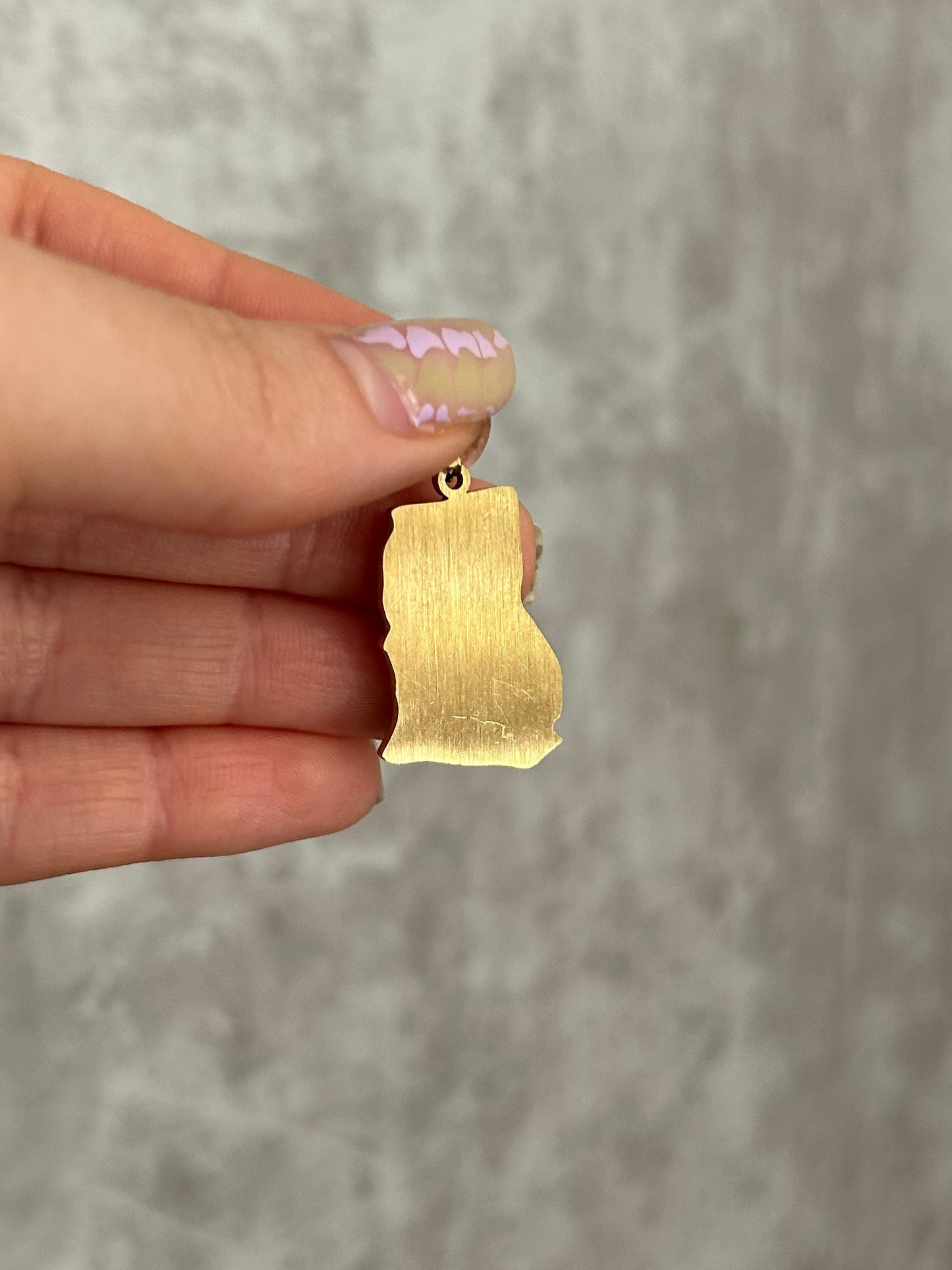 Hand holding a gold pendant against a neutral background