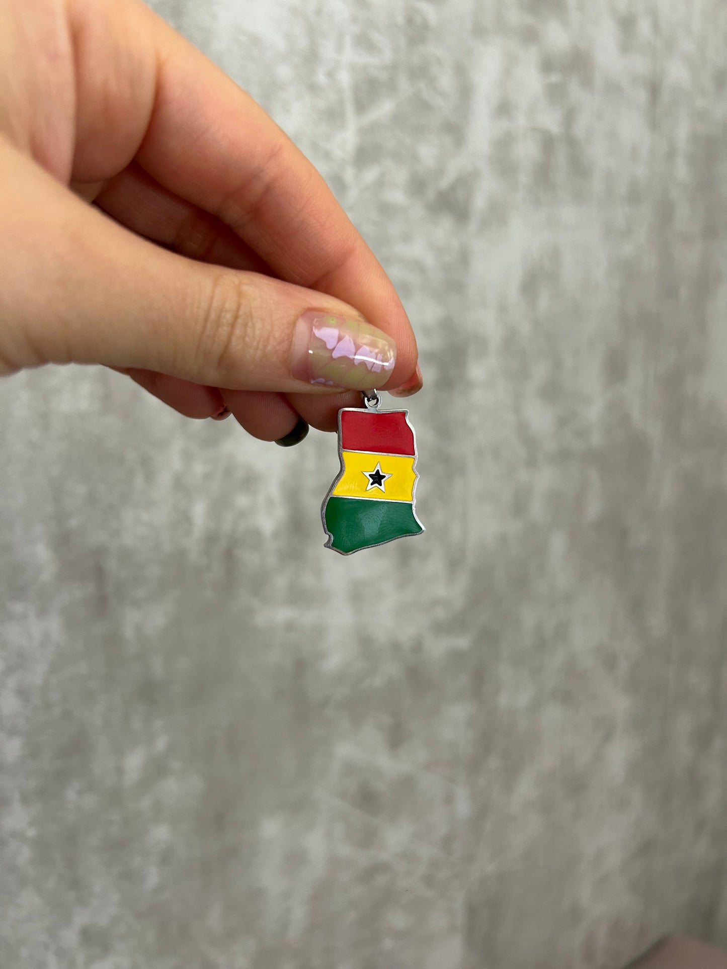 Hand holding a Ghana flag-shaped pendant against a gray background