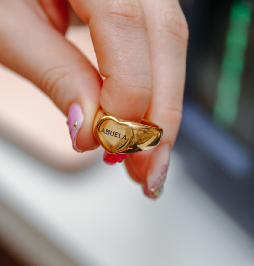 Woman with manicured nails wearing engraved heart-shaped grandma abuela ring – Mother’s Day gift jewelry 