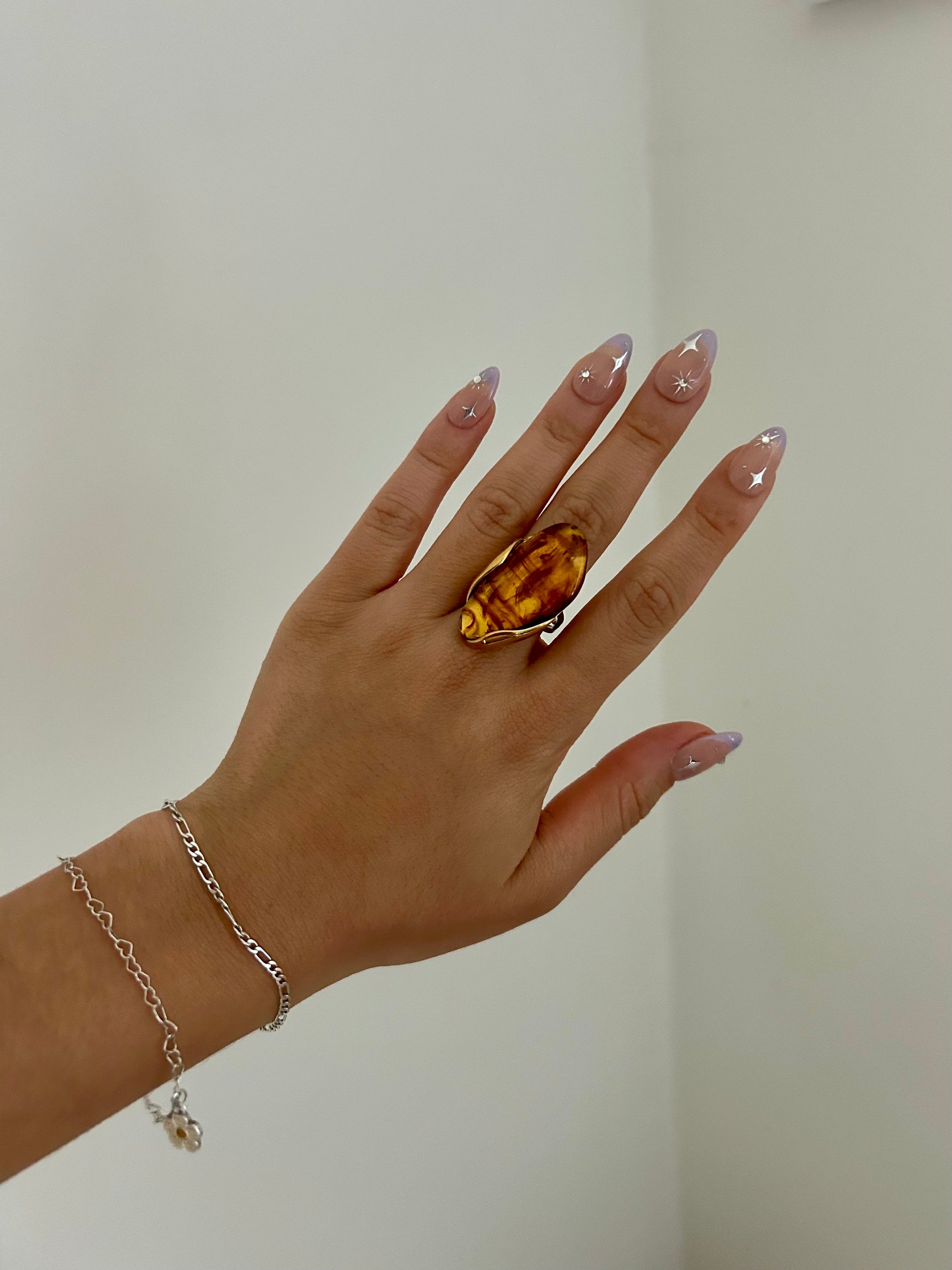 Hand wearing a large amber ring with a plain background