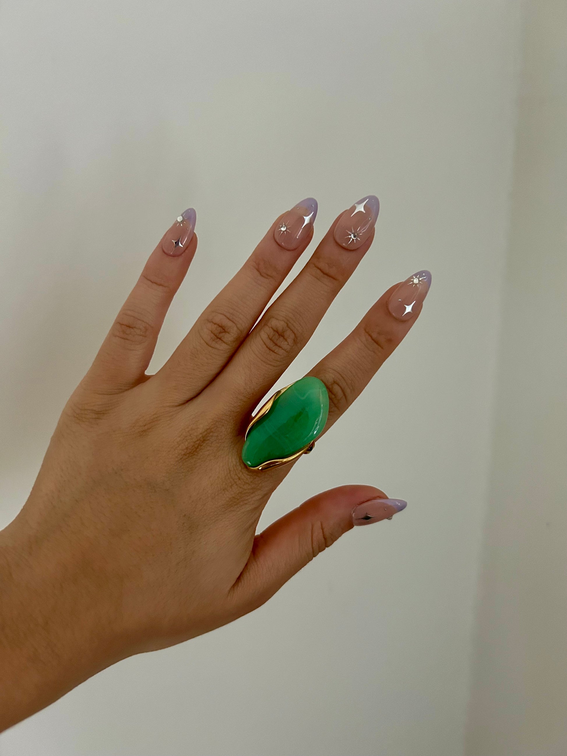 Hand wearing a green ring on a plain background
