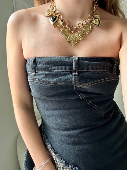 Person wearing a gold necklace and denim strapless top against a neutral background