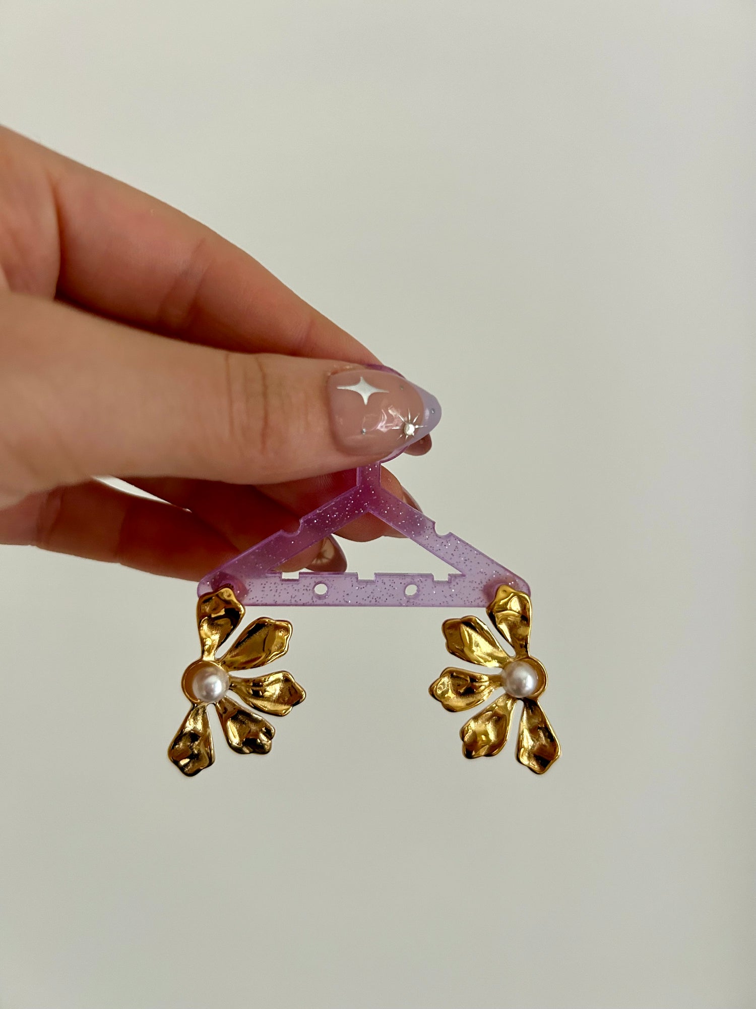 Gold floral earrings on a pink stand held by a hand with star-shaped nail polish.
