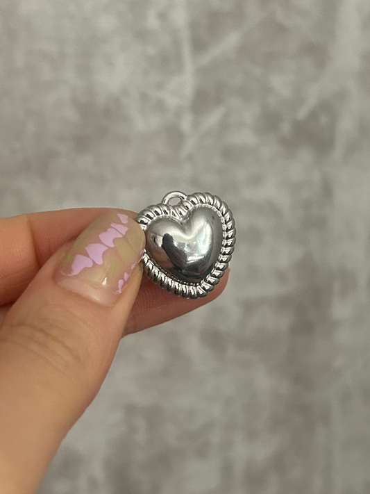 Silver heart-shaped object held by a hand against a gray background
