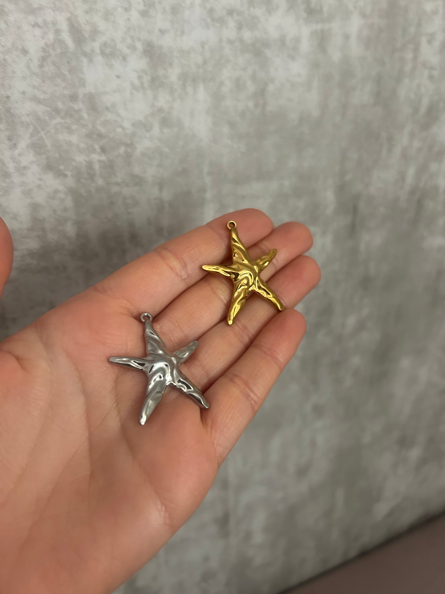 Hand holding a silver and a gold star-shaped pendant against a gray background