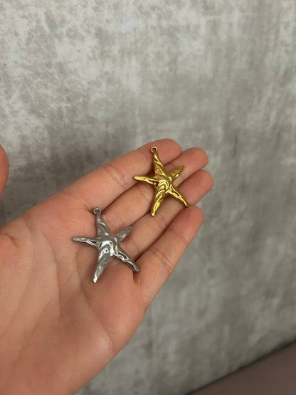Hand holding a silver and a gold star-shaped pendant against a gray background
