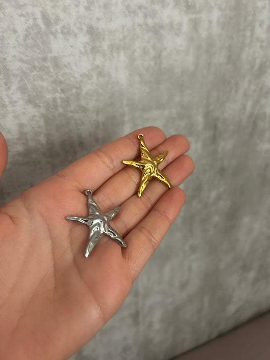 Hand holding a silver and a gold star-shaped pendant against a gray background
