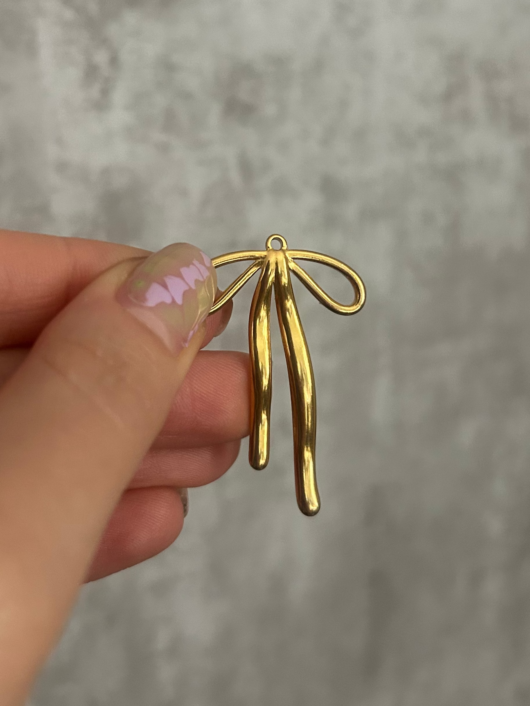 Gold bow-shaped charm held by a hand against a gray background