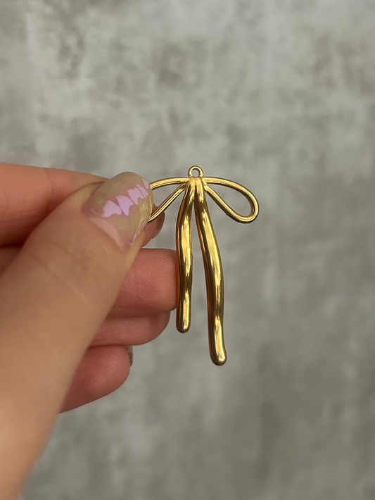 Gold bow-shaped charm held by a hand against a gray background