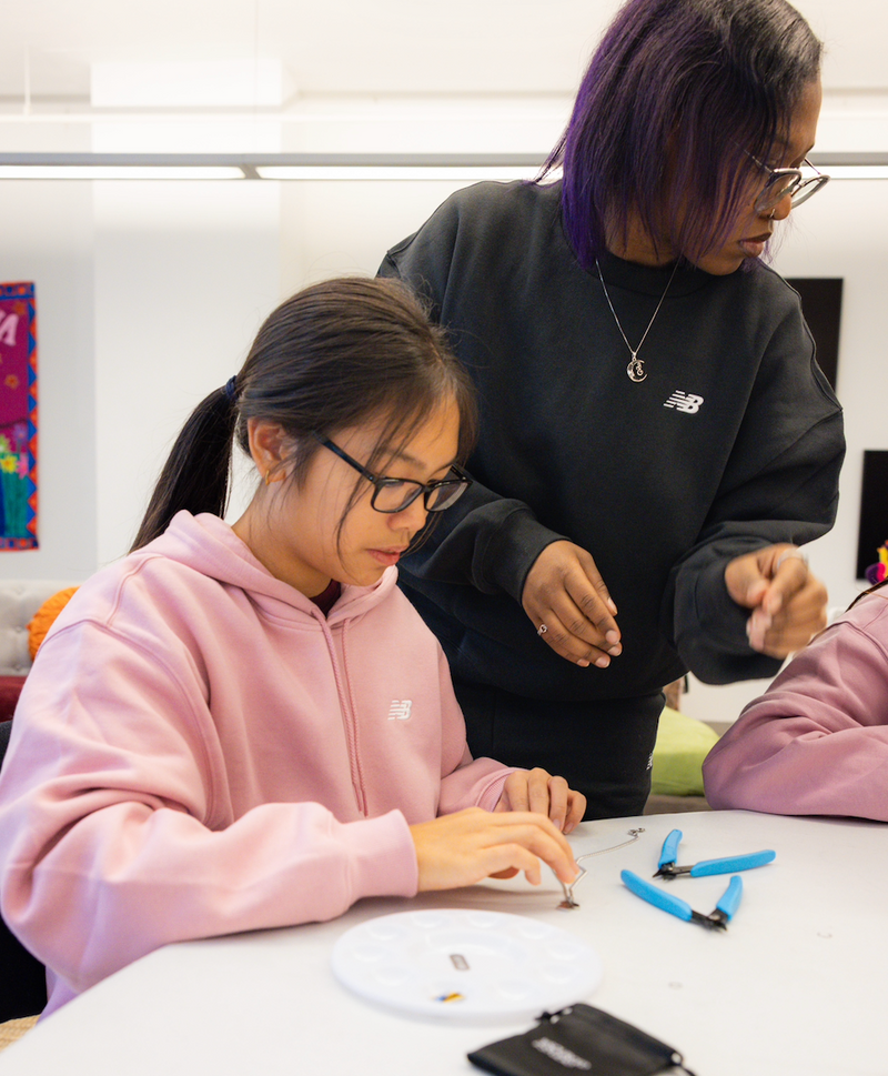 Two people working on a jewelry project at a table with tools