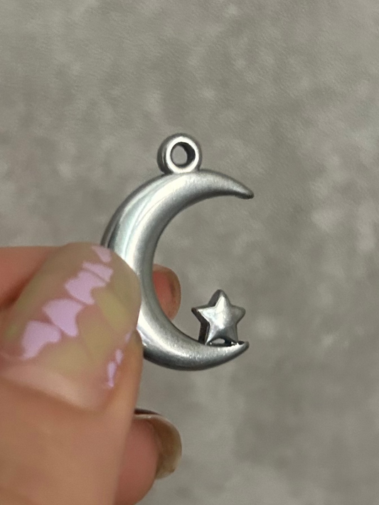 Silver moon and star charm held between fingers against a gray background