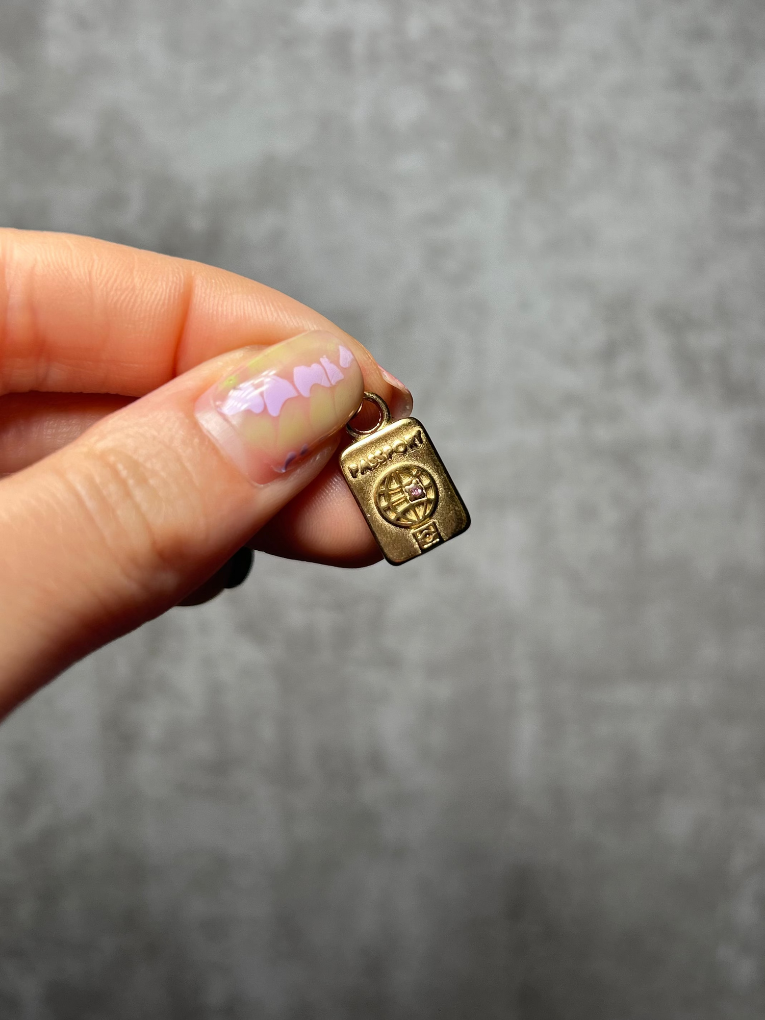 Gold charm held by a hand against a gray background