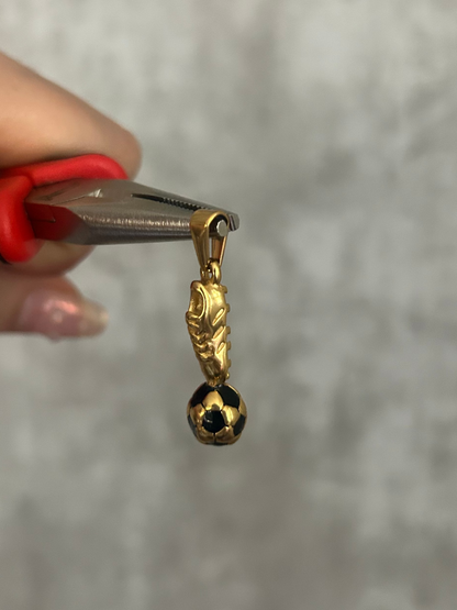 Gold charm with a black bead held by a hand using pliers against a neutral background