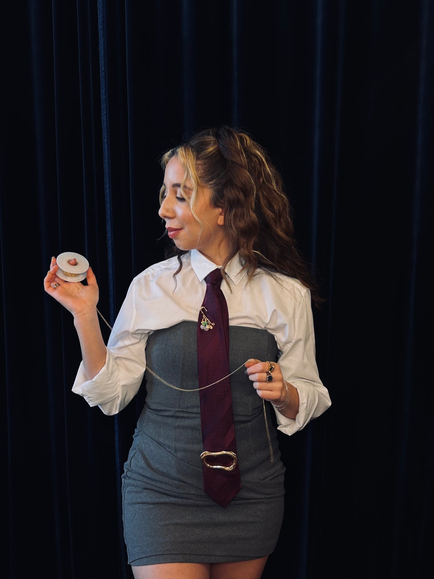 Woman in a chic outfit holding a jewelry roll against a black curtain