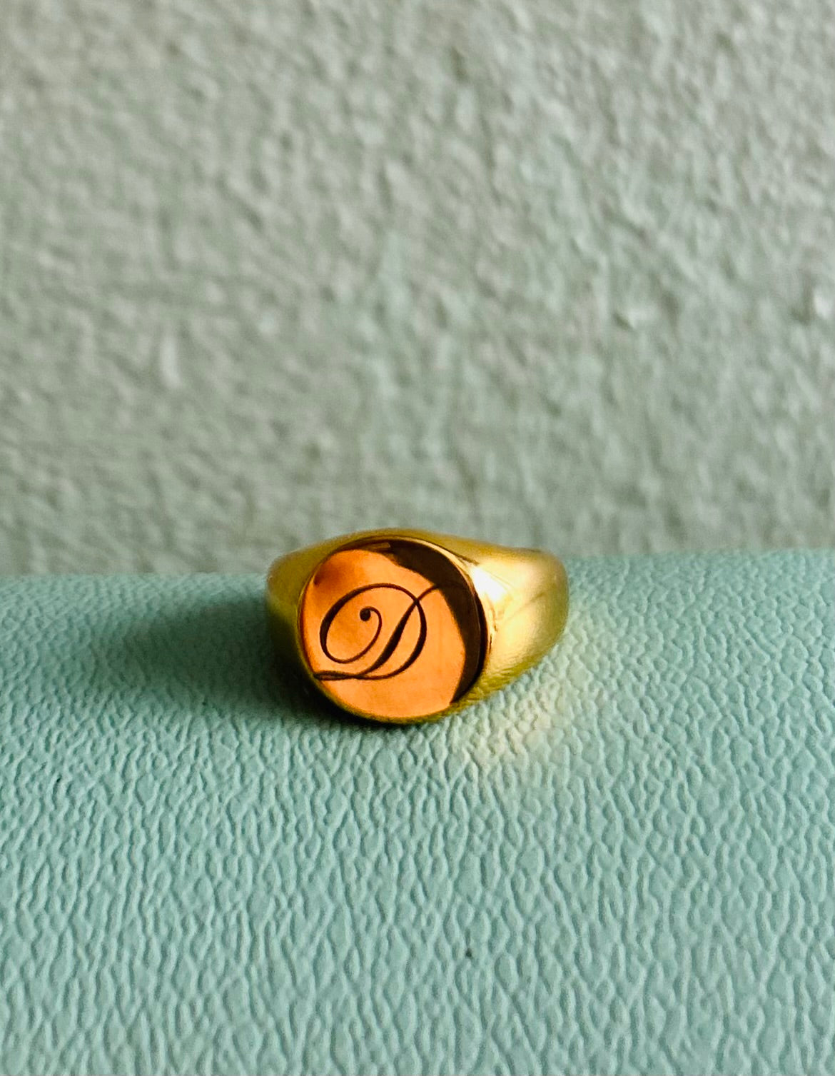 Gold ring with a monogram on a light green surface