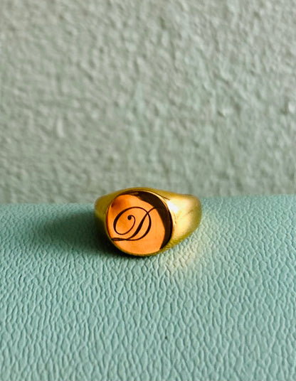 Gold ring with a monogram on a light green surface
