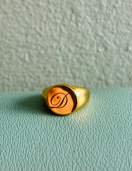 Gold ring with a monogram on a light green surface