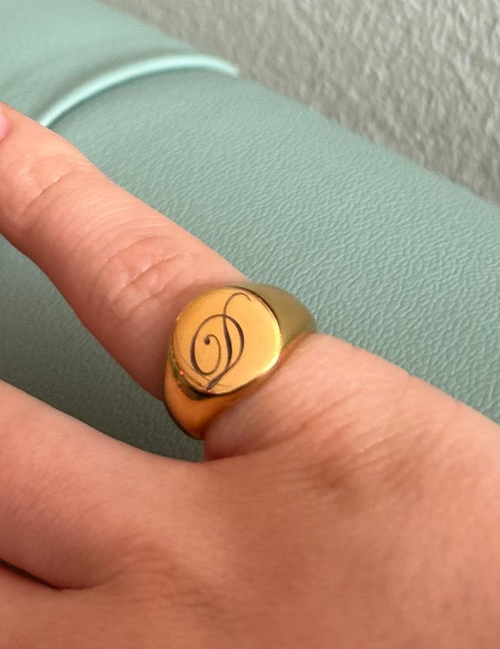Hand wearing a gold ring with a symbol on a light green surface.