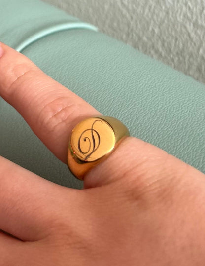 Hand wearing a gold ring with a symbol on a light green surface.
