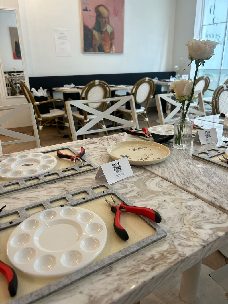 Jewelry setup with charm trays, work mats, and pliers on a marble table in a dining area.