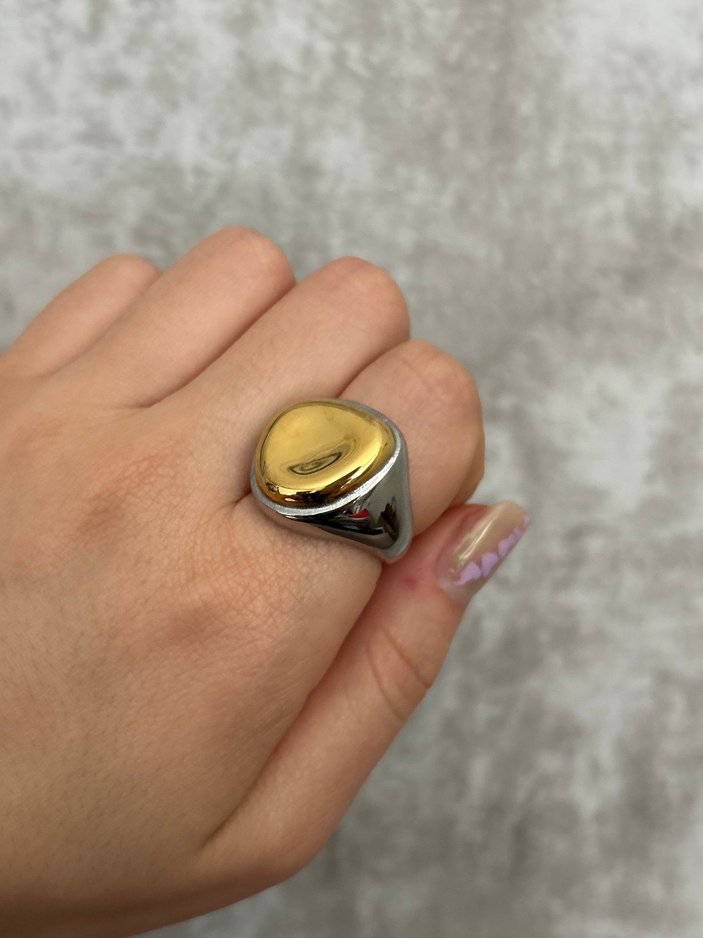 Hand wearing a gold ring on a gray textured background